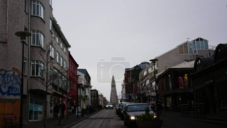Foto de Reykjavik, Islandia - 27 de marzo de 2018: Una calle del centro estacionada con autos y Hallgrimskirkja al fondo bajo un cielo nublado antes de la pandemia - Imagen libre de derechos