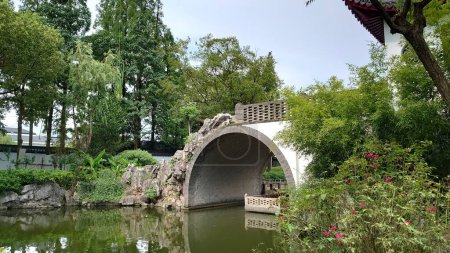Téléchargez les photos : Zhujiajiao Ancienne ville, Shanghai, Chine - 25 juillet 2019 : Pont rocheux chinois sur un étang entouré d'arbres dans le jardin Kezhi - en image libre de droit