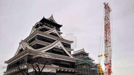 Téléchargez les photos : Kumamoto, Japon - 01.26.2020 : Vue de face du château de Kumamoto en cours de reconstruction après le séisme de 2016 avec des échafaudages et une grue en vue sous un ciel nuageux - en image libre de droit