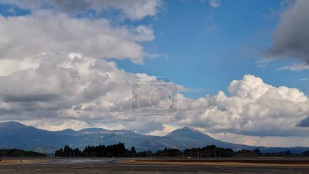 Photo for Kagoshima Airport, Japan - 01.30.2020: View of the runway from the terminal with a mountain range and trees at the back and clouds in the blue sky - Royalty Free Image