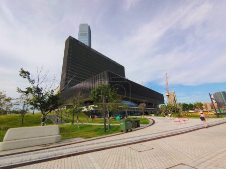 Téléchargez les photos : Hong Kong - 08.29.2021 : Vue latérale grand angle du musée Mplus avec pelouse et visiteurs marchant sur la passerelle sous un ciel bleu pendant la pandémie - en image libre de droit