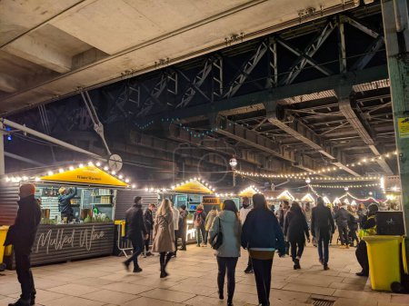 Photo for London, UK - 12.21.2021: People browsing the busy Christmas Market under Hungerford Bridge and Golden Jubilee Bridges in Southbank at night - Royalty Free Image