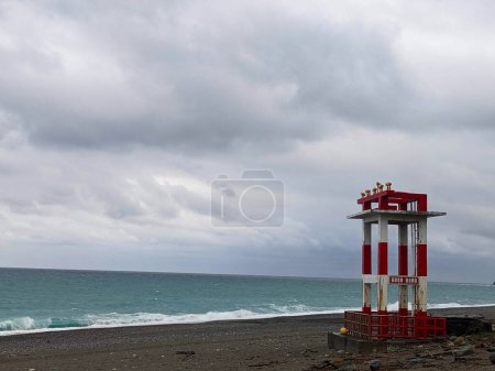 Foto de Hualien, Taiwán - 11.26.2022: Una estructura metálica roja y blanca con cuernos de advertencia en la vacía playa de Qixingtan frente al ondulado Océano Pacífico en un día tormentoso bajo las nubes durante la pandemia - Imagen libre de derechos