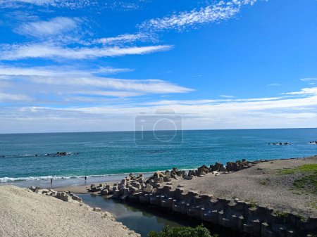 Photo for Hualien, Taiwan - 11.27.2022: Jian Stream leading to the Pacific Ocean via a beach with tetrapods on the side and people enjoying the beach on a sunny day under a blue sky during the pandemic - Royalty Free Image