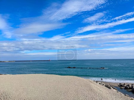 Photo for Hualien, Taiwan - 11.27.2022: Jian Stream leading to the Pacific Ocean via a beach with tetrapods and people enjoying the beach under a sunny blue sky during the pandemic with a lighthouse in sight - Royalty Free Image