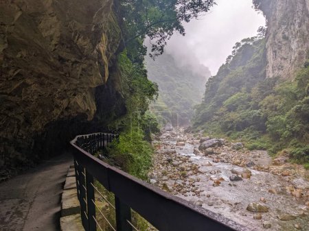 Photo for Taroko, Taiwan - 11.26.2022: Dark and empty Shakadang Trail goes under a cliff alongside Liwu River in a mist during the pandemic before 403 earthquake on a rainy day - Royalty Free Image