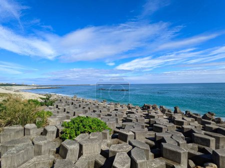 Photo for Hualien, Taiwan - 11.27.2022: A beach half-filled with tetrapod and sandy at the other side facing the Pacific Ocean with a lighthouse in sight under a sunny blue sky during the pandemic - Royalty Free Image