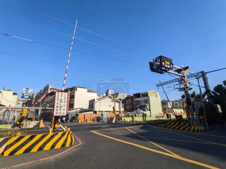 Photo for Tainan, Taiwan - 12.02.2022: A motorist rode across an opened level crossing with the barrier gates lifted upward and railroad in sight into a neighbourhood street on a sunny day during the pandemic - Royalty Free Image
