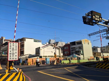 Photo for Tainan, Taiwan - 12.02.2022: A motorist riding across an opened level crossing with the barrier gates lifted upward and railroad in sight into a neighbourhood street on a sunny day during the pandemic - Royalty Free Image