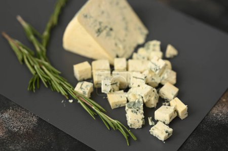 Un queso azul de olor en una tabla gris y trozos cortados con romero. Foto de alta calidad
