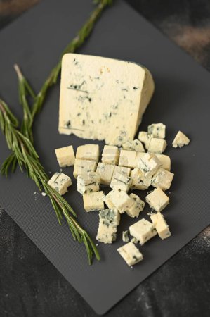 Un fromage bleu dor sur une planche grise et couper les morceaux avec du romarin. Photo de haute qualité