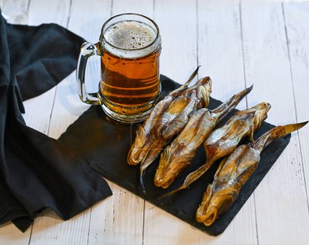 Dried salted sea goby on a paper with glass bear. Traditional snack for beer. Close-up. High quality photo