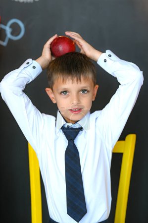 Cute schoolboy sitting on cube with apple on his head. High quality photo