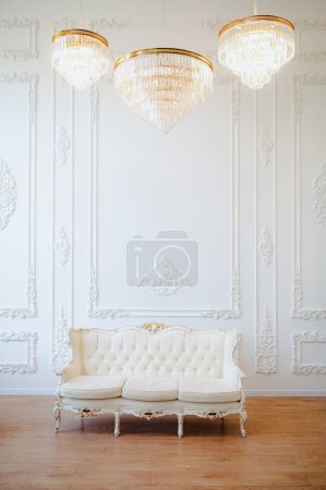 Photo for White baroque sofa against a white wall, large three chandeliers on the ceiling. High quality photo - Royalty Free Image