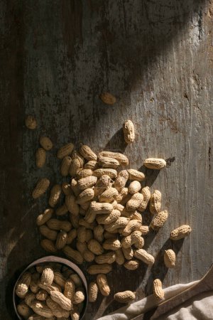 Photo for Pile of unpeeled peanuts on a wooden background with old cup, also known as groundnut, goober, pindar or monkey nut,taken directly from above with copy space - Royalty Free Image