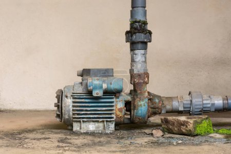 Foto de Vieja bomba de agua eléctrica oxidada con tuberías de suministro de agua de pvc, espacio de copia - Imagen libre de derechos