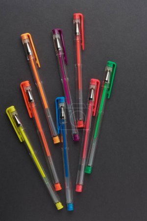 Téléchargez les photos : Huit stylos colorés dispersés sur la surface du papier noir, concept de papeterie scolaire et de bureau, pris d'en haut avec espace de copie - en image libre de droit