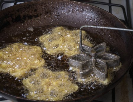 fabrication de biscuits kokis ou rosettes, aliments sri lankais croustillants à base de farine de riz et de lait de coco, vue rapprochée de la friture de kokis dans une casserole avec un moule en forme de fleur, plat traditionnel