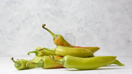 Téléchargez les photos : Pile de poivrons de banane sur le dessus de table blanc, capsicum annuum, piment long, forme incurvée avec doux en chaleur et saveur acidulée et légèrement sucrée, prise sur fond texturé avec espace de copie - en image libre de droit