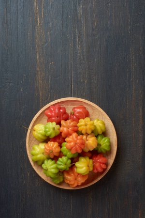 Photo for Surinam cherries, eugenia uniflora, aka pitanga, brazilian or cayenne cherry, vibrant colorful fruits on wooden plate, isolated on black rustic background surface with copy space - Royalty Free Image