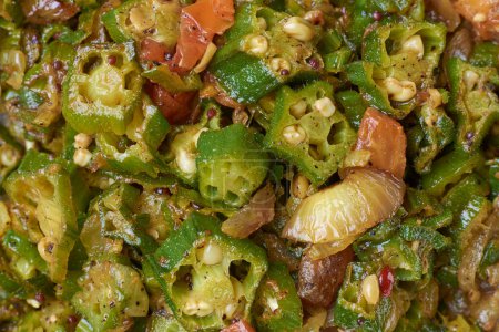 stir fried okra or okro dish close-up, aka lady's fingers, tempered vegetarian curry cooked with spices in full frame, food background, onions, tomatoes and mustard seeds added