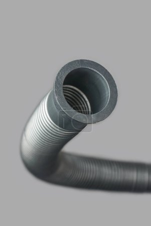 Nahaufnahme von flexiblem Wellrohr oder Schlauch, Kunststoff- oder PVC-Flexi-Rohrverbindung isoliert grauen Hintergrund, in Sanitärsystemen für Wasserversorgung und Entwässerung in selektivem Fokus verwendet