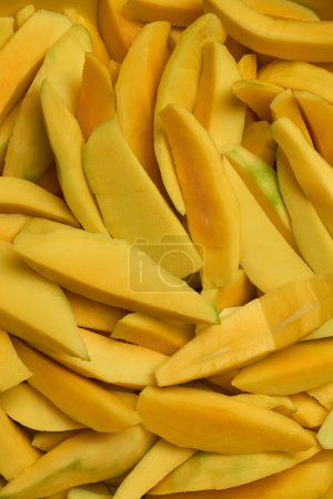 sliced pieces of peeled ripe mangoes for various culinary uses, pile of cut skin removed tropical fruit for desserts salads chutneys smoothies and beverages, food background from above