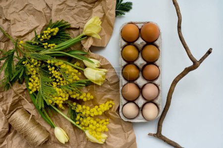 Téléchargez les photos : Bouquet déplié de tulipes sur papier kraft près des œufs dans un porte-oeuf en papier sur fond blanc. concept de printemps - en image libre de droit