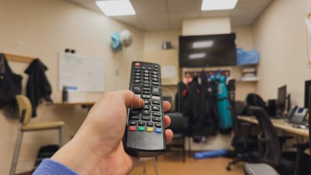 Photo for A person holding a remote control while sitting on a couch watching television. The sedentary lifestyle is countered by exercise equipment in the background, while the latest technology like smart TV - Royalty Free Image