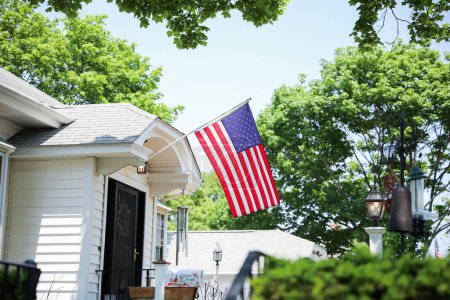 Photo for US flag proudly displayed in front of an American house symbolizes patriotism, national identity, and love for one's country. It represents unity, freedom, and the values upon which the United States was built - Royalty Free Image