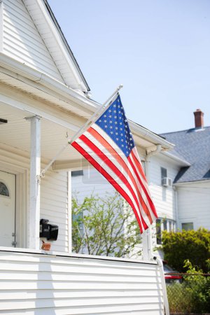 Photo for US flag proudly displayed in front of an American house symbolizes patriotism, national identity, and love for one's country. It represents unity, freedom, and the values upon which the United States was built - Royalty Free Image