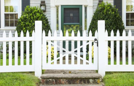 Téléchargez les photos : Clôture en bois blanc devant la maison verte, clôture blanche avec des feuilles vertes et des fleurs blanches. - en image libre de droit