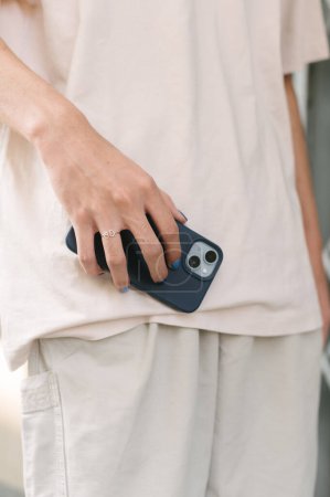 Téléchargez les photos : Crop homme anonyme en blanc vêtements décontractés tenant téléphone portable moderne dans les mains avec des ongles bleus - en image libre de droit