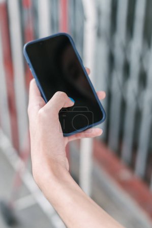 Foto de Un tipo irreconocible con uñas azules que navega por el teléfono móvil con pantalla negra en el fondo borroso de la calle de la ciudad - Imagen libre de derechos
