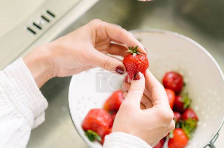 Foto de Alto ángulo de hembra anónima con fresa roja fresca en las manos preparando comida saludable para el desayuno en la cocina - Imagen libre de derechos