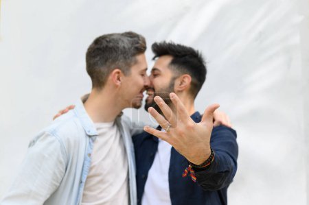 Photo for Side view of cheerful Hispanic homosexual man demonstrating ring and smiling while embracing boyfriend after proposal - Royalty Free Image