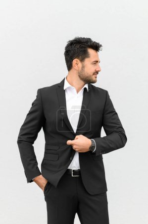 Téléchargez les photos : Entrepreneur masculin confiant en costume chic debout avec les mains dans les poches et regardant loin sur fond blanc en studio - en image libre de droit