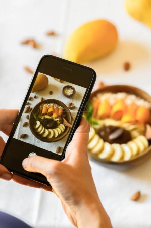 Photo for High angle of crop anonymous person taking photo on cellphone of bowl with delicious homemade healthy breakfast - Royalty Free Image