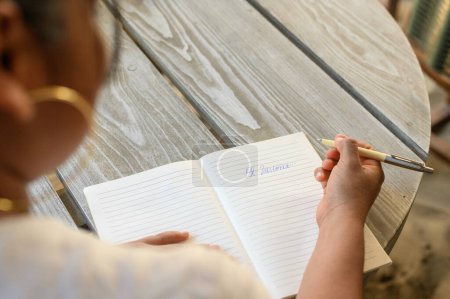 Hohe Schnittwinkel anonyme weibliche Schreibnotizen in Planer mit Stift, während sie am Holztisch in der Cafeteria im Freien sitzen