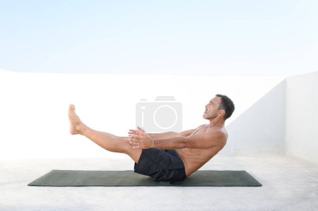 Foto de Un hombre de mediana edad sin camisa haciendo ejercicio en casa en la terraza. Muscular 50 años bien parecido hombre blanco está haciendo ejercicio en el suelo de su casa haciendo una rutina de ABS y el entrenamiento de sus músculos principales. - Imagen libre de derechos