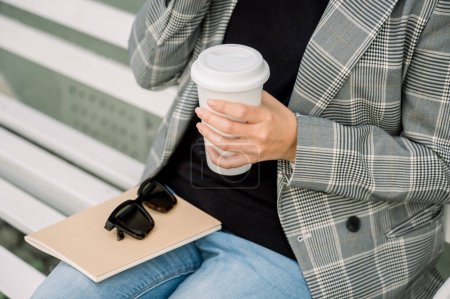 Téléchargez les photos : D'en haut de la récolte femelle anonyme en vêtements décontractés assis sur le banc avec tasse de café et ordinateur portable - en image libre de droit