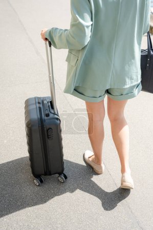Téléchargez les photos : De haut de la récolte femelle anonyme en vêtements décontractés avec valise debout sur la route dans la ville - en image libre de droit