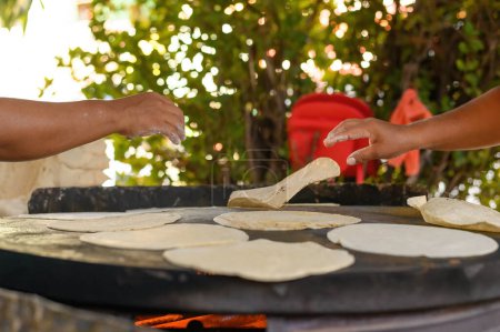 Foto de Cultivar chefs irreconocibles poniendo trozo de masa en la estufa mientras se preparan tortillas en el campo en México - Imagen libre de derechos