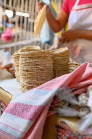 Téléchargez les photos : Pile de tortillas fraîchement fabriquées sur le comptoir près de la récolte cuisinière anonyme travaillant au stand dans le marché local pendant la journée - en image libre de droit