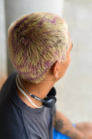 Téléchargez les photos : Vue arrière d'un homme méconnaissable avec des cheveux teints blonds, un casque et un tatouage assis sur la rue - en image libre de droit
