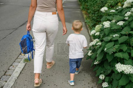 Foto de Madre irreconocible en ropa casual con la mochila en la mano, lleva a su hijo a clase. De vuelta a la escuela. Foto de alta calidad - Imagen libre de derechos