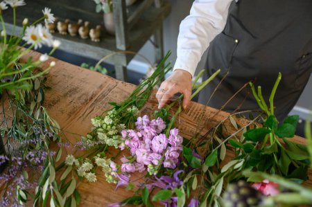 Téléchargez les photos : Grand angle de culture spécialiste anonyme dans tablier debout à la table en bois et l'organisation de fleurs à fleurs tendres sur le marché floral - en image libre de droit