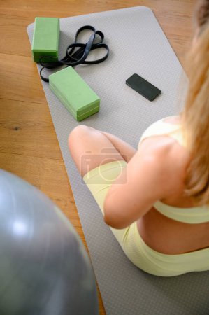 Photo for Back view of Young pregnant woman is doing exercise on the exercise mat next to her, exercise ball smartphone in Living room at home - Royalty Free Image
