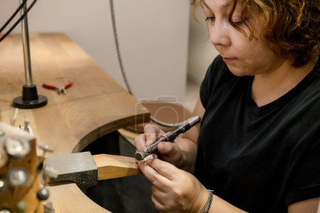 Téléchargez les photos : Vue latérale de l'artisan adulte concentré assis à l'espace de travail, bague de meulage et de travail dans l'atelier de bijoux. concept d'entreprise - en image libre de droit