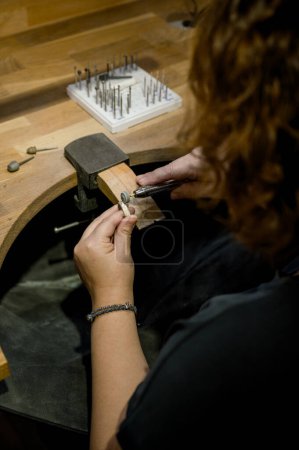 Téléchargez les photos : Vue latérale mains de femme méconnaissable assis à l'orfèvre espace de travail, bague de broyage et de travail dans l'atelier de bijoux. concept d'entreprise - en image libre de droit